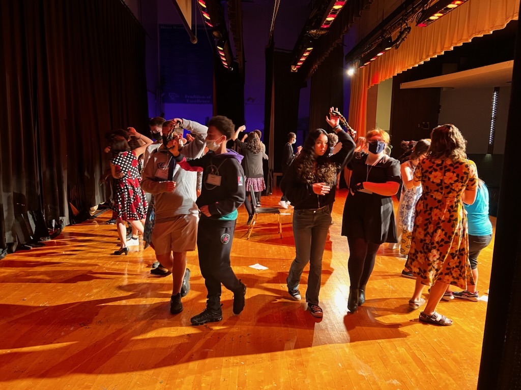 Approximately 20 Middle school students dancing in pairs in a circle on a large stage.