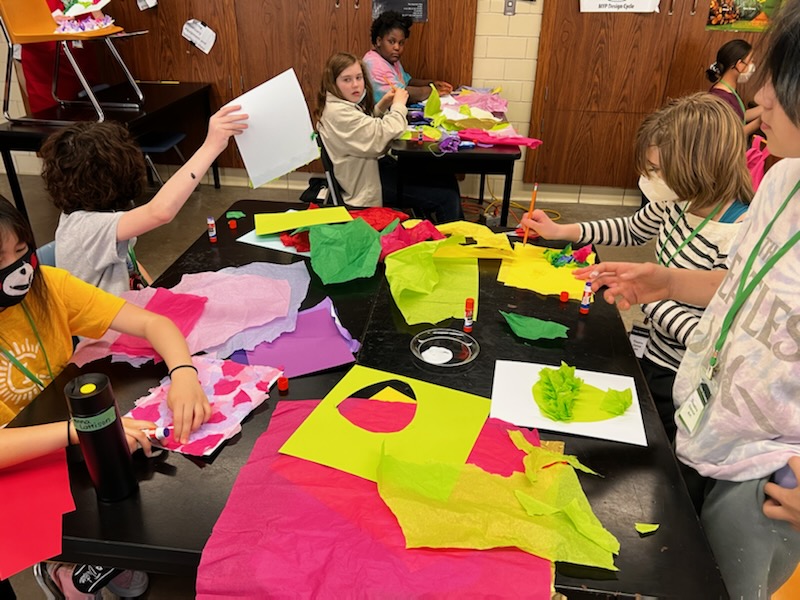Classroom setting with seven young students creating art using colorful tissue paper and glue sticks