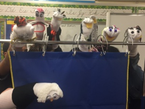 Seven sock puppets behind a blue curtain on a metal rod