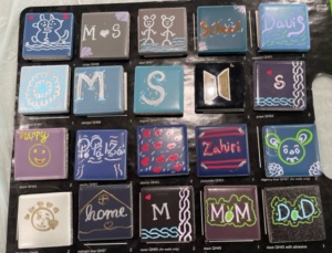 Twenty ceramic tiles all painted differently. Some have letters, some have names, some have patterns and some have faces