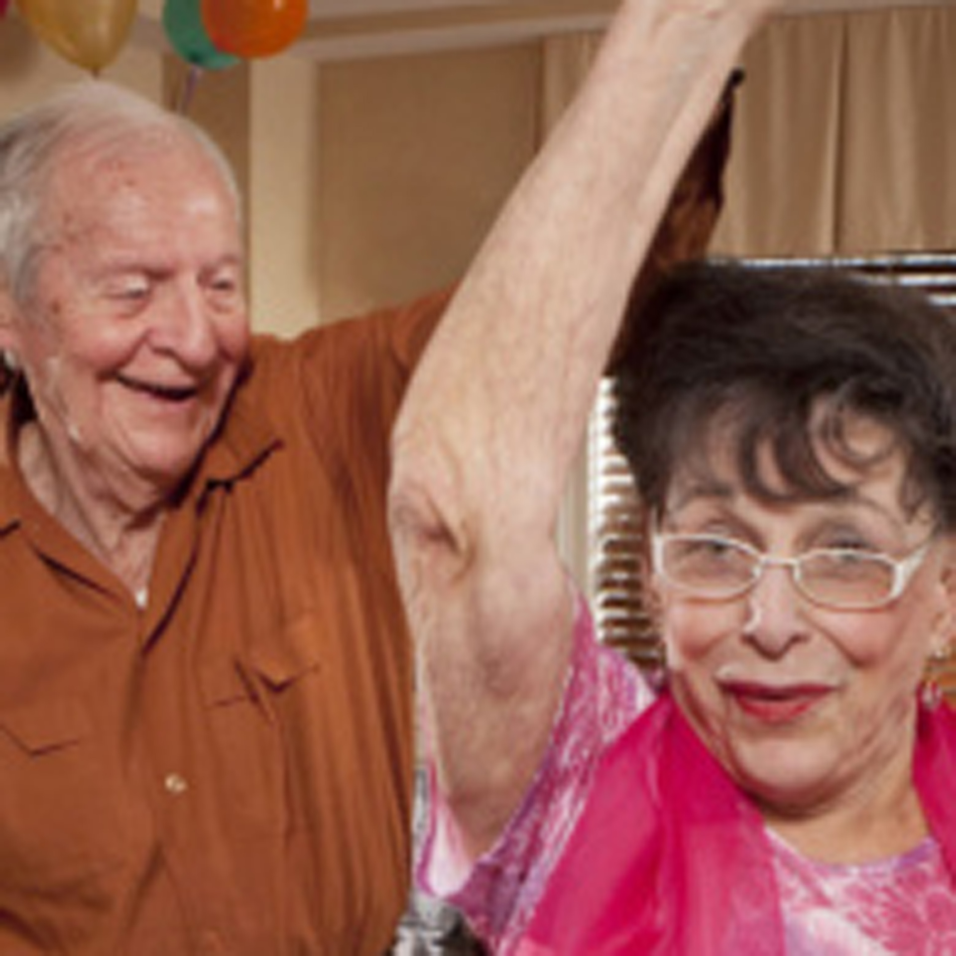 Older man looking at older woman, both are smiling. The man is holding the woman's arm up over her head